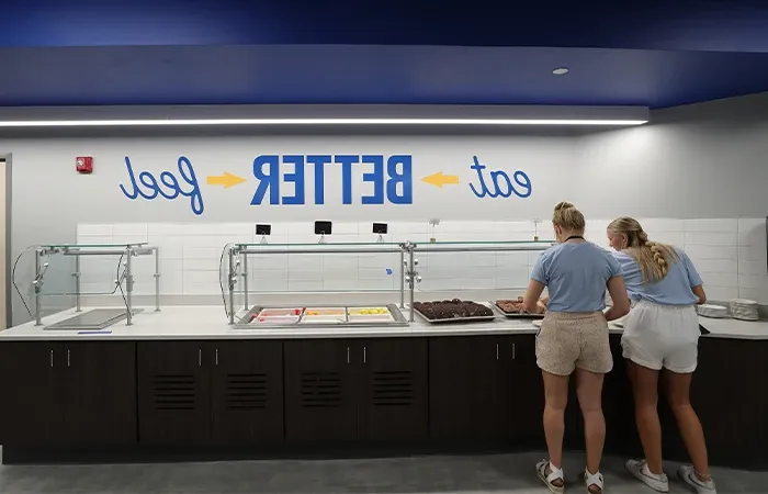 students serve themselves food in front of a sign that says eat better, feel better